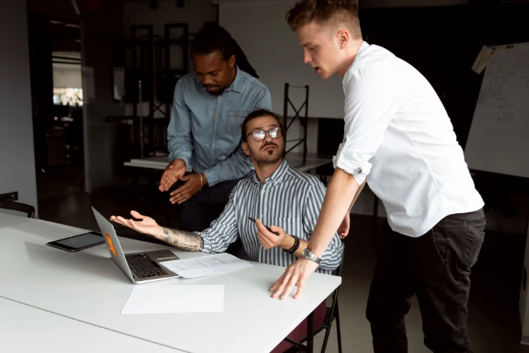 Three colleagues reviewing a laptop screen together in an office — agencies are the ones fielding the hard questions from local business owners as Google's rules shift